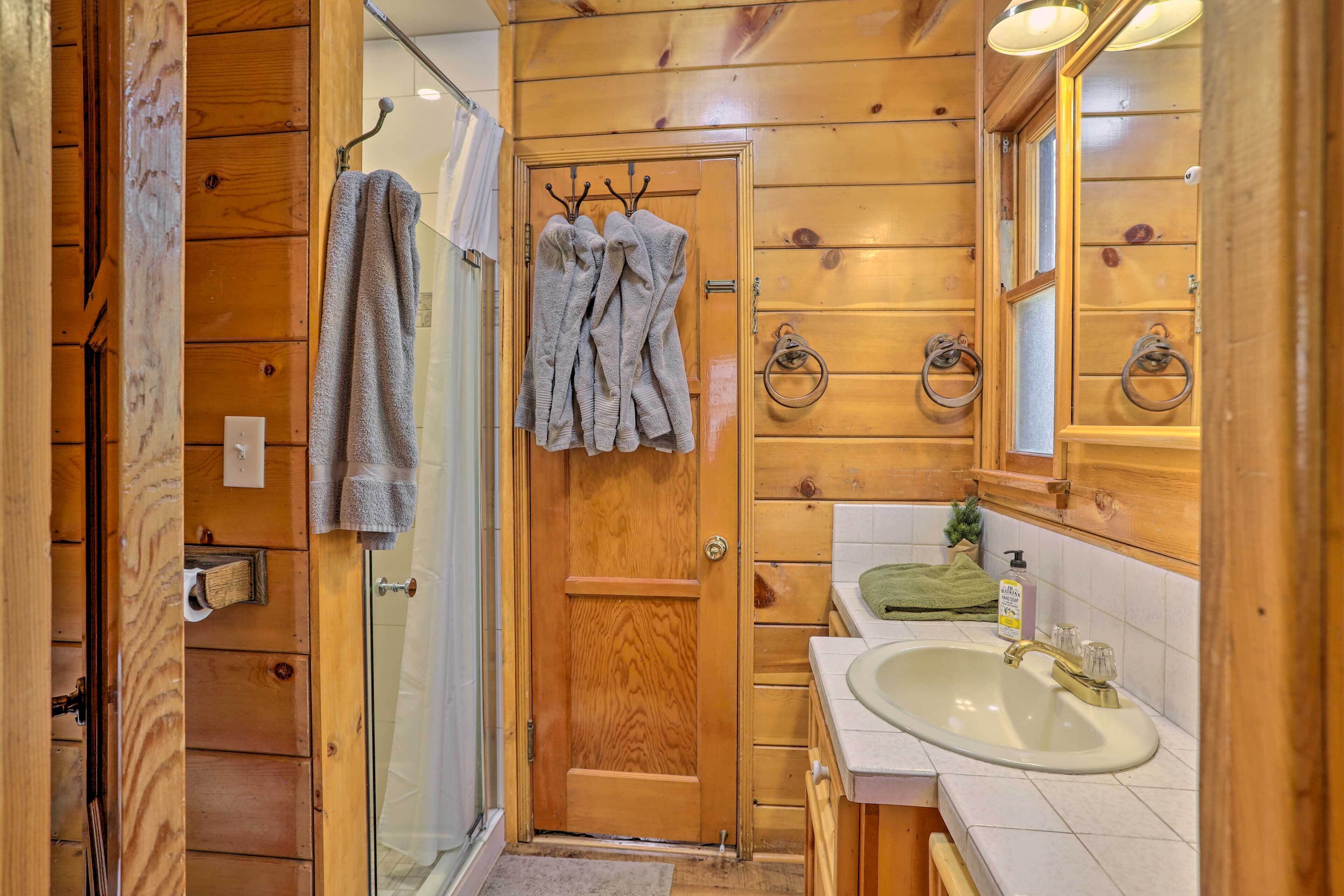 A wooden cabin bathroom with a glass shower, a sink with a mirror, and towels hanging on hooks.