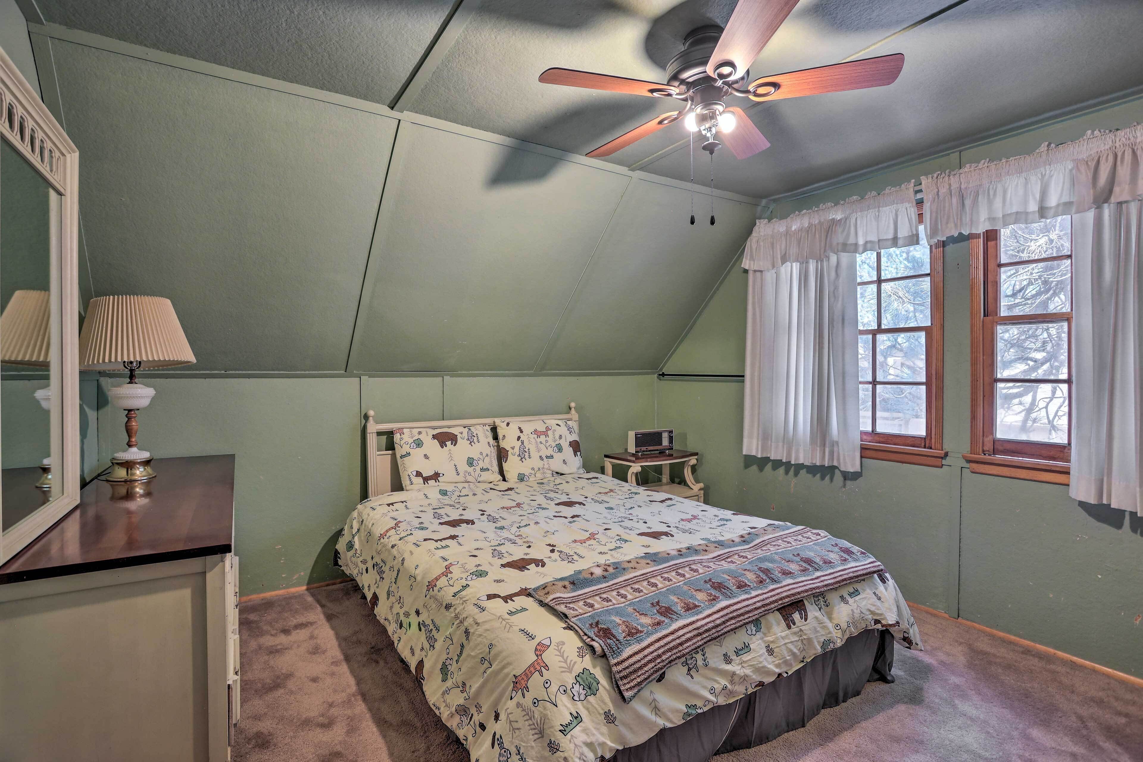 Un dormitorio con cama, ventilador de techo, mesita de noche, lámpara y ventana con cortinas.