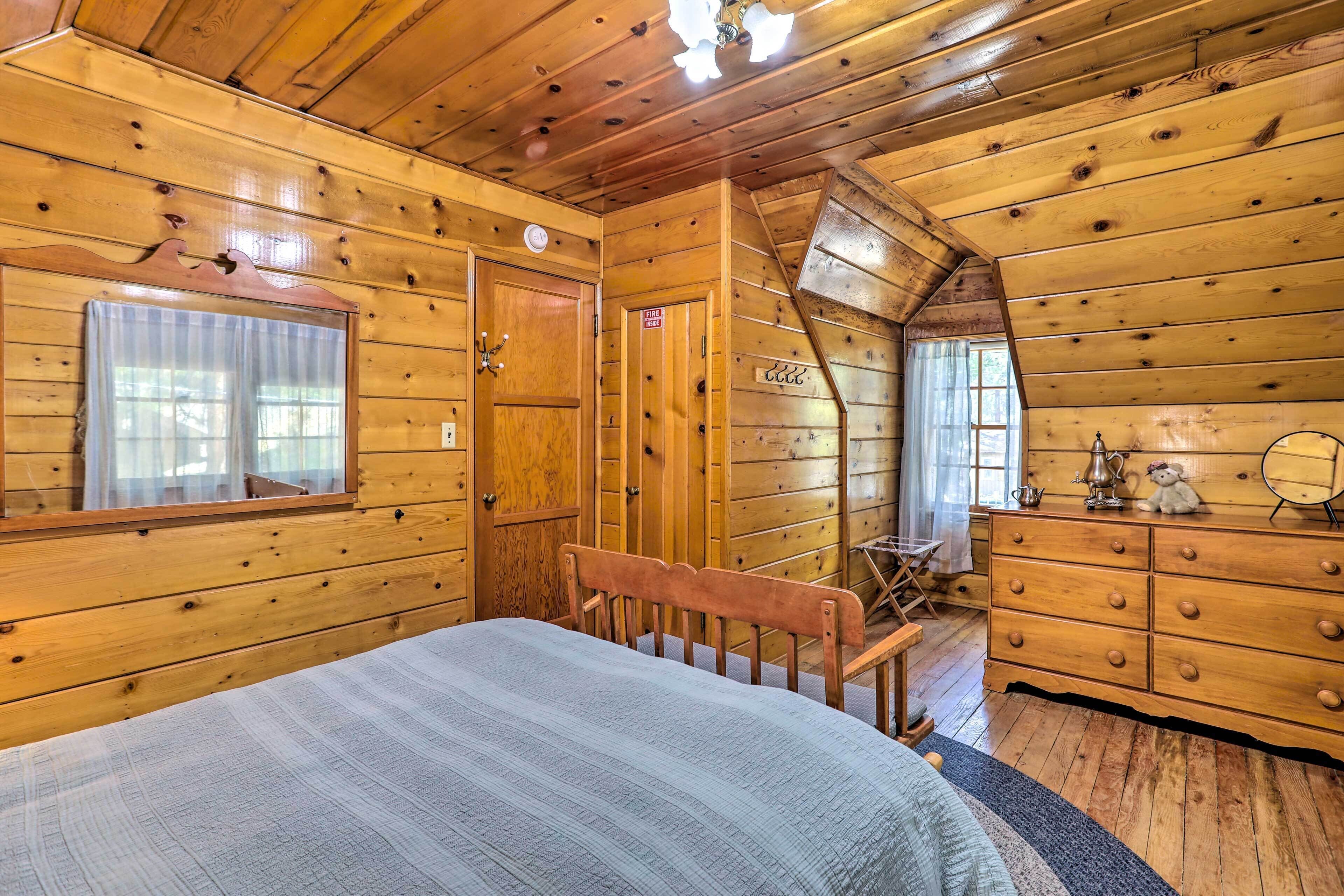 Een slaapkamer in een houten chalet, met een bed, een dressoir en een kleine tafel met stoel.