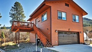 A two-story log cabin with a balcony, a garage, and a clear view of the surrounding forest.