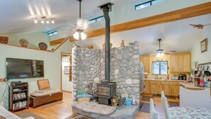 A cozy living room with a stone fireplace, wooden floors, a sofa, and a television. - Secluded Placerville Cabin w/ Deck: Walk to River! (Placerville)