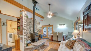 A cozy living room with a fireplace, a sofa, and a dining area. - Secluded Placerville Cabin w/ Deck: Walk to River! (Placerville)