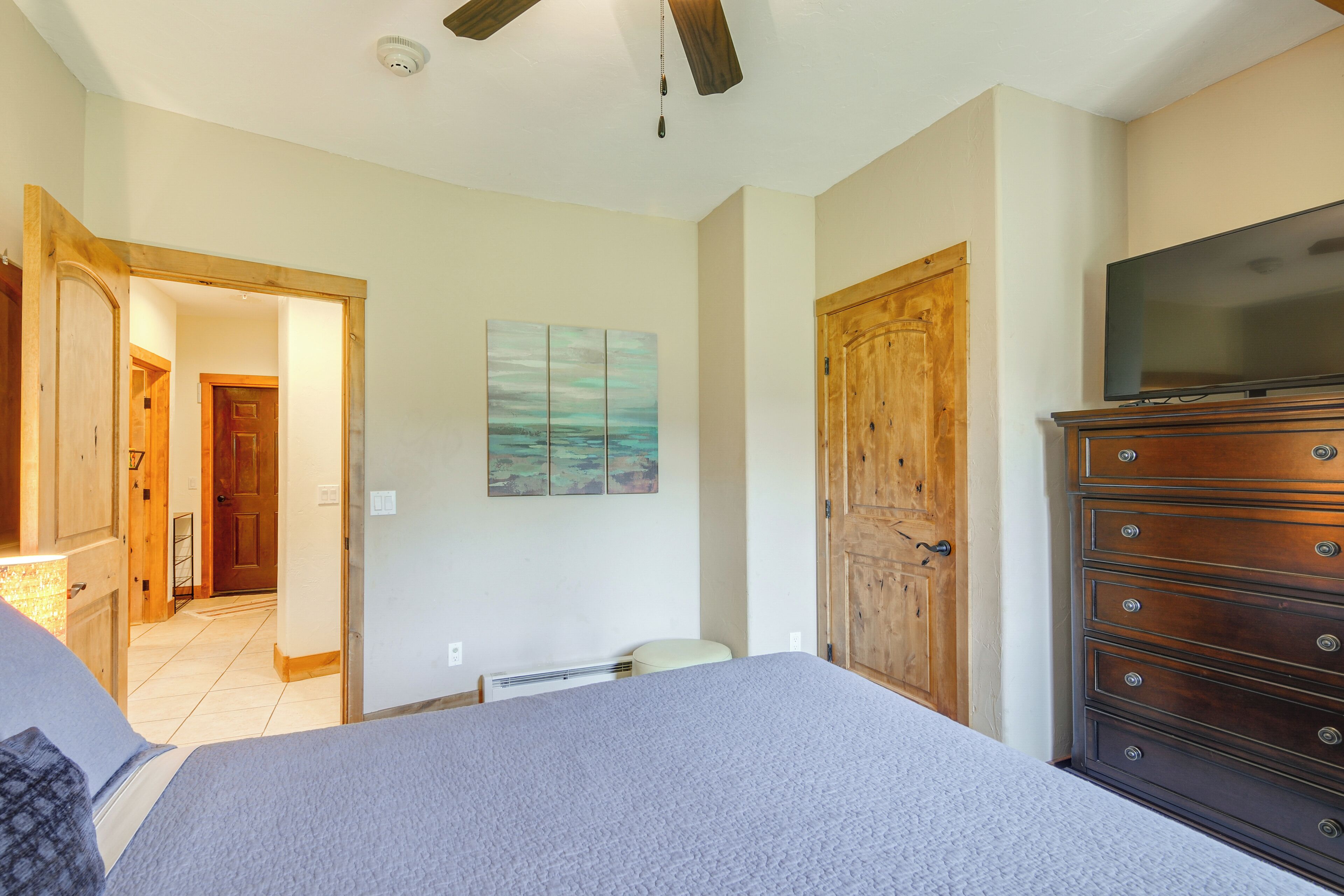 A bedroom with a bed, a dresser, a television, and a painting on the wall.