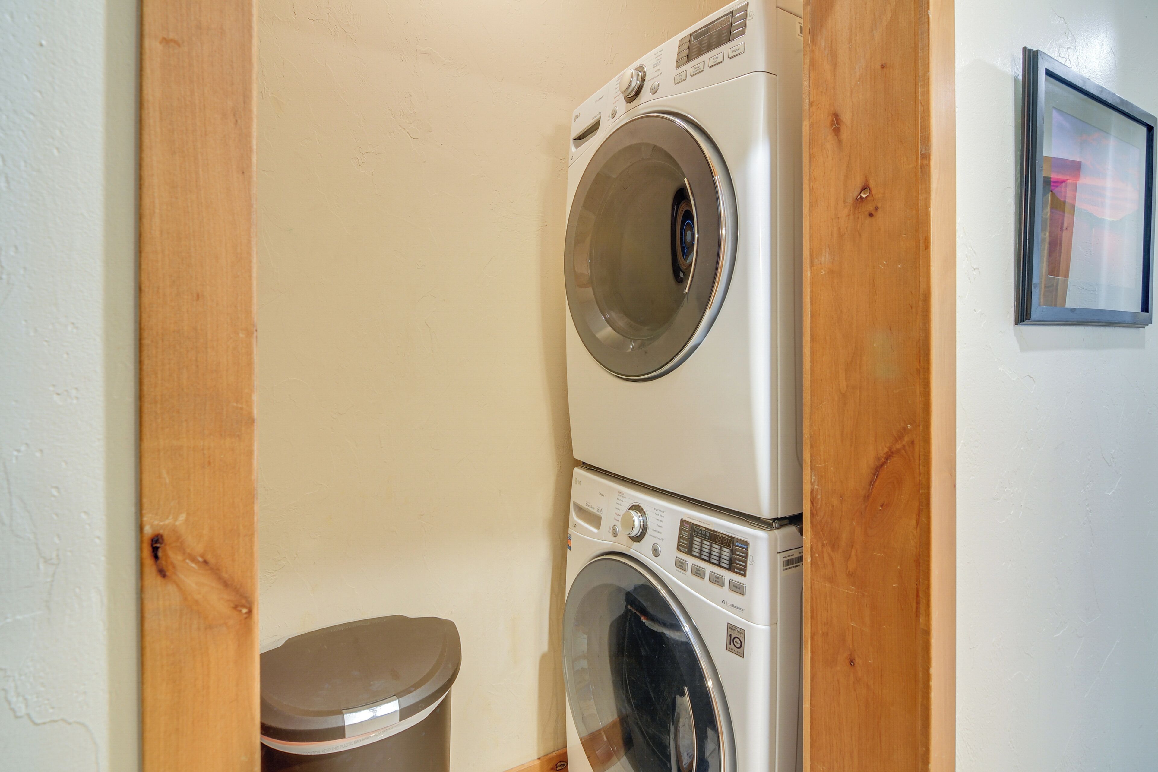 A laundry area with two stacked washing machines and a trash bin.