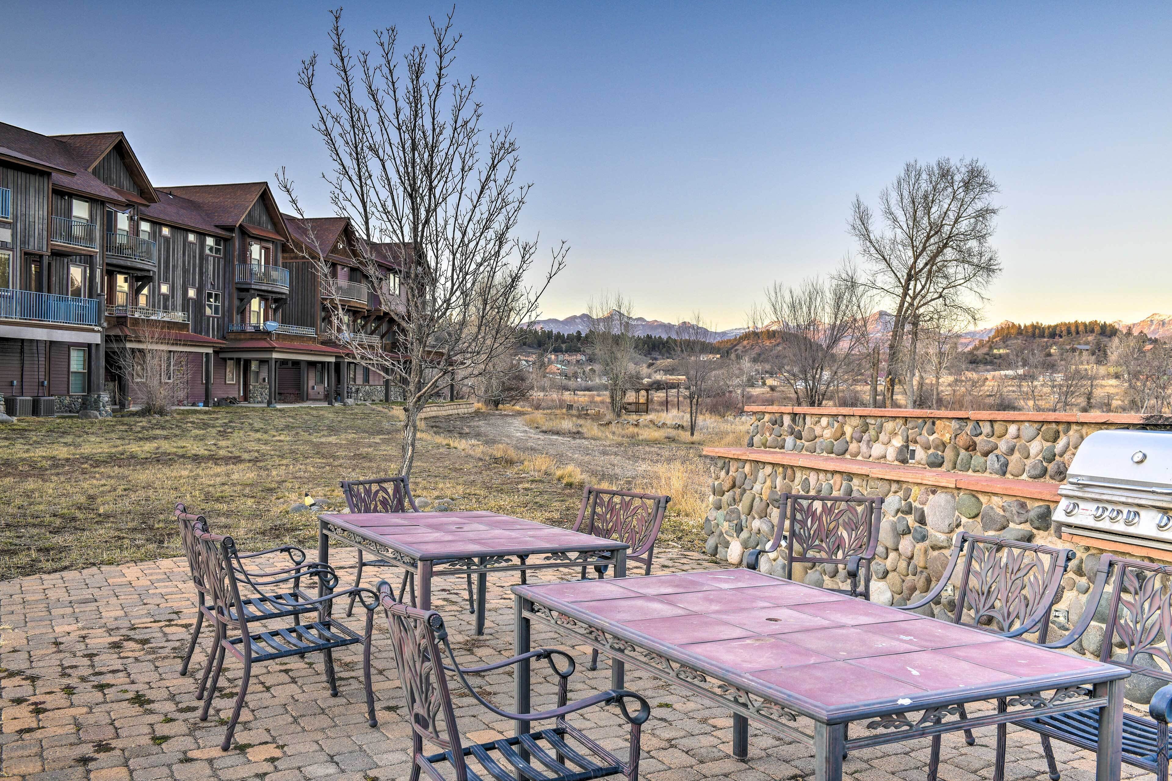 A patio area with outdoor seating and a barbecue grill, surrounded by a stone wall and a view of mountains.