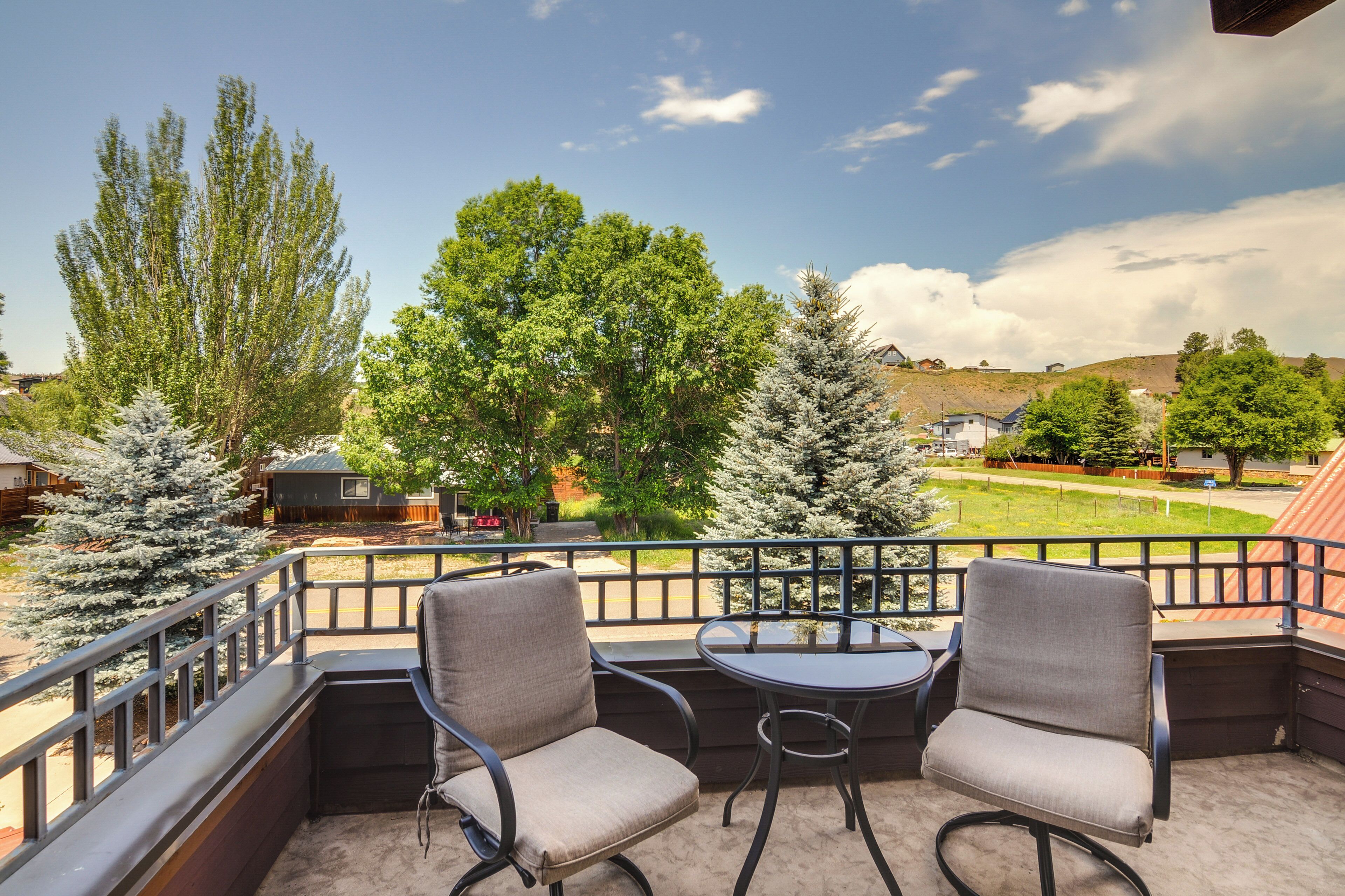A balcony with two chairs and a table, overlooking a green landscape with trees and a hill.