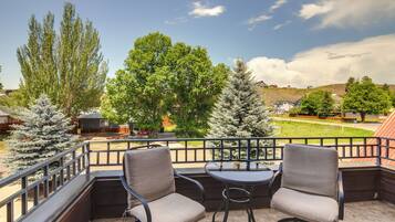 A balcony with two chairs and a table, overlooking a green landscape with trees and a hill.