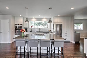A modern kitchen with a central island, bar stools, stainless steel appliances, and pendant lighting.