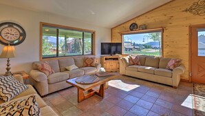 Una sala de estar acogedora con dos sofás, una mesa de centro, un televisor y ventanas amplias que ofrecen vistas al exterior.
