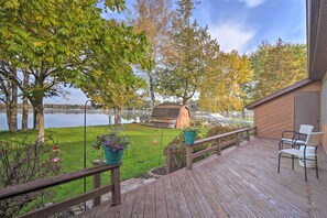 A wooden deck with outdoor furniture, a grassy area, trees, and a body of water in the background.