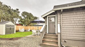 A residential backyard with a patio area, a small shed, and a covered seating area under an umbrella. - Chic Lincoln City Retreat on Oregon Coast (Lincoln City)