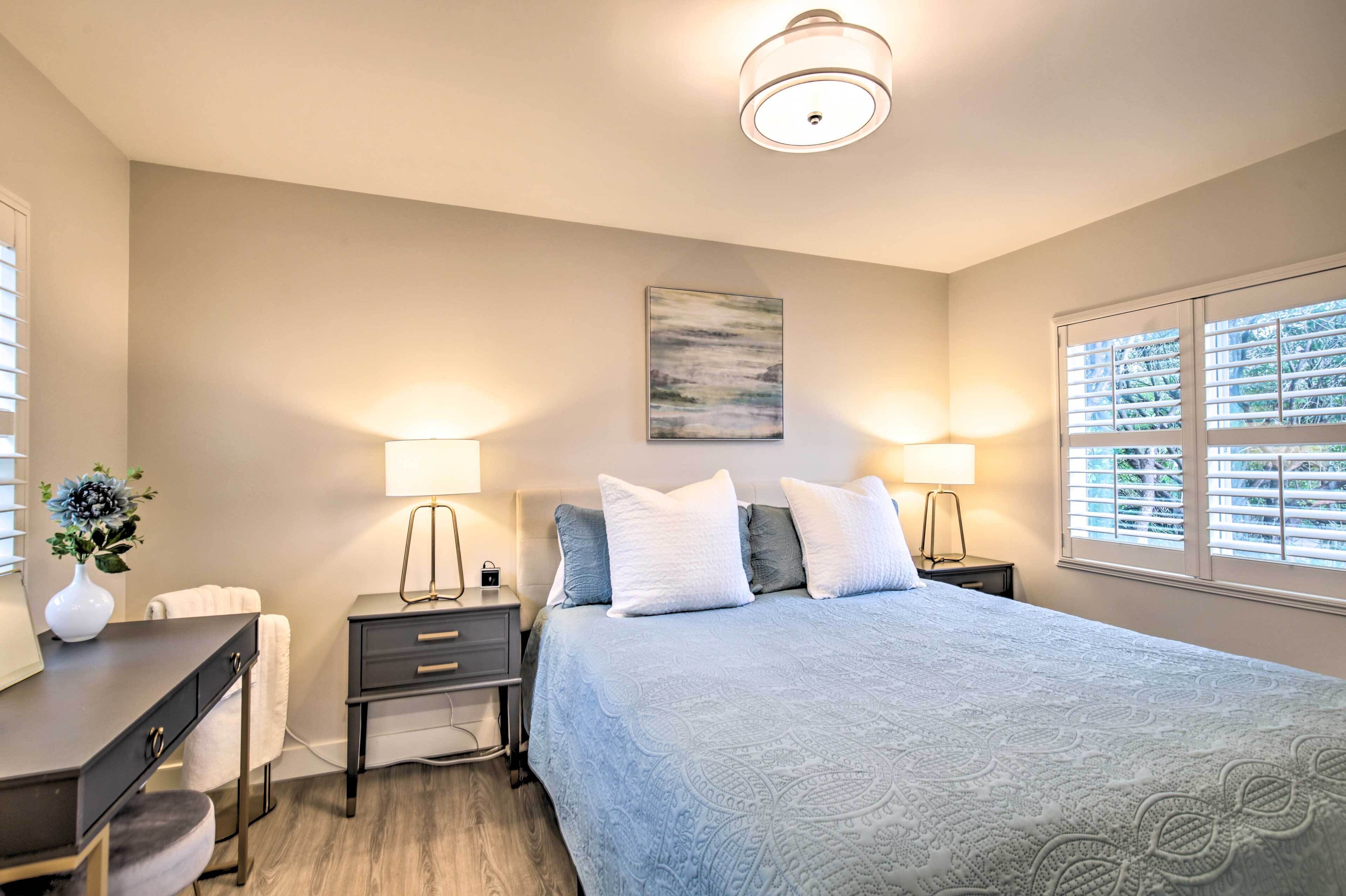 A bedroom with a bed, bedside tables, lamps, a painting, and a window with blinds.