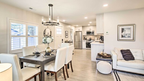 A modern kitchen with stainless steel appliances, a dining area with a dark wooden table, and a living area with a white sofa and a round ottoman. - Chic Lincoln City Retreat on Oregon Coast (Lincoln City)
