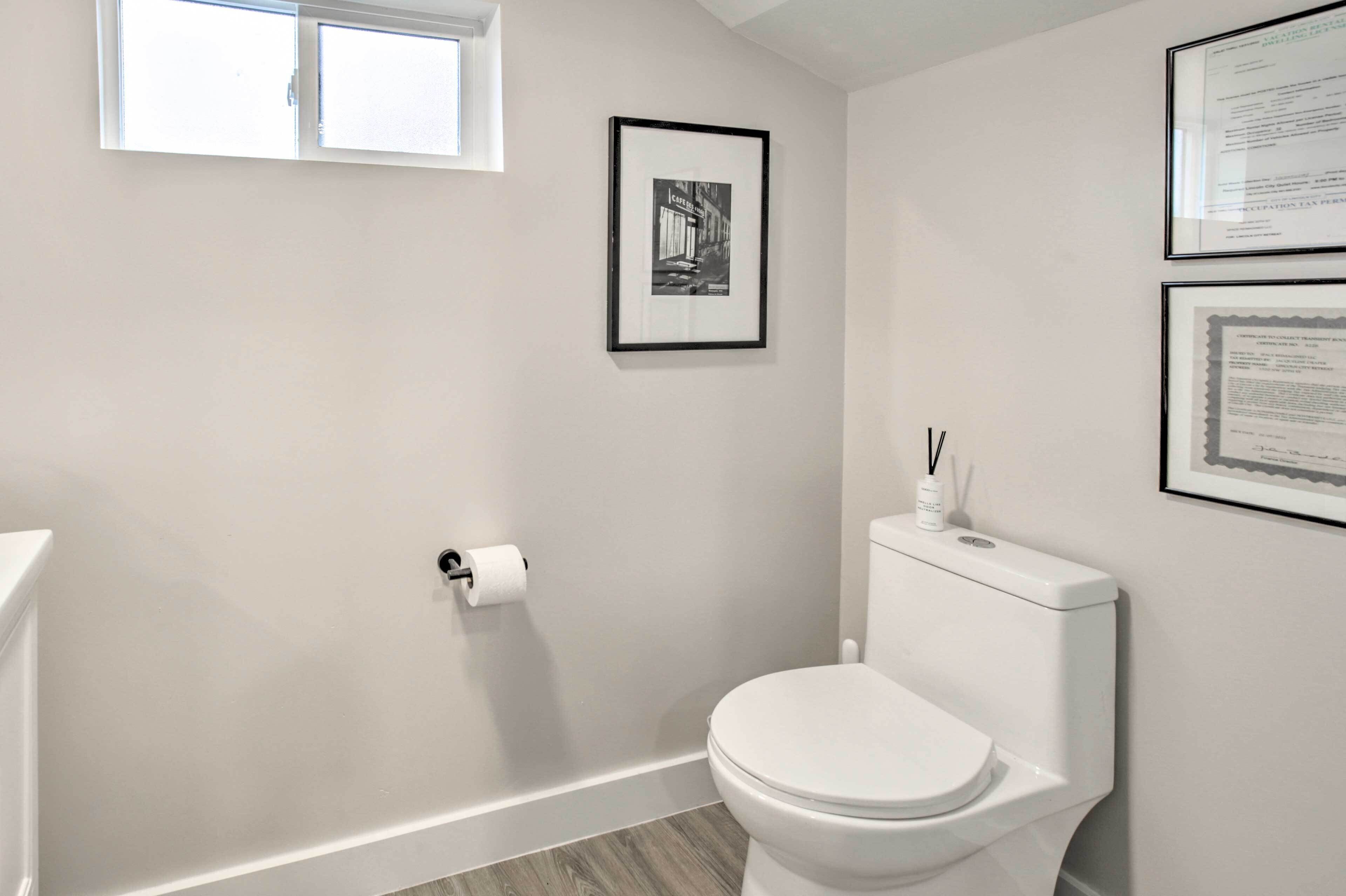 A bathroom with a toilet, a framed picture on the wall, and a window.