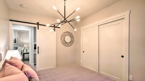 A bedroom with a bed, a ceiling light fixture, a door, and a wall-mounted circular object. - Chic Lincoln City Retreat on Oregon Coast (Lincoln City)