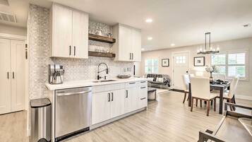 A modern kitchen with white cabinetry, a stainless steel dishwasher, and a dining area with a table and chairs.