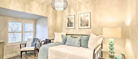 Un dormitorio con cama, una silla, una mesita de noche con lámpara y dos cuadros en la pared.