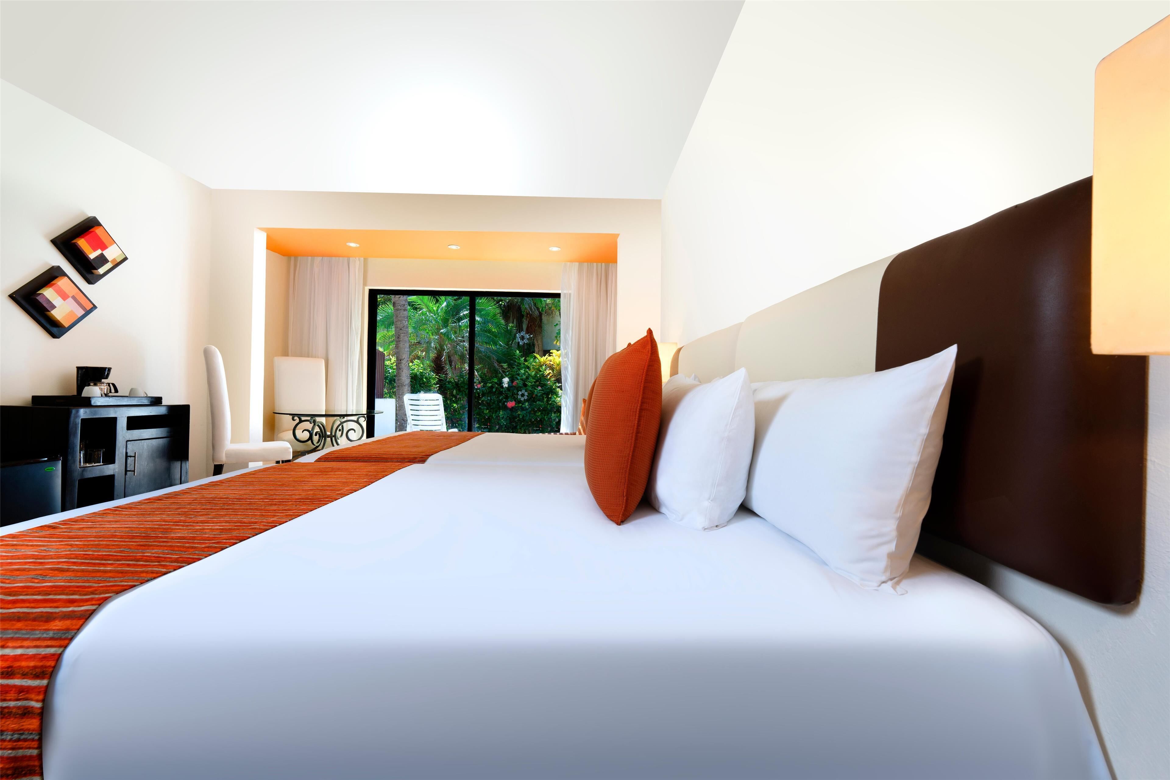 Une chambre d’hôtel moderne, dotée d’un grand lit, d’un bureau, d’une chaise et offrant une vue sur la verdure par la fenêtre.