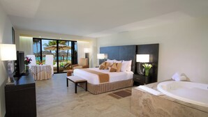 Ein geräumiges Hotelzimmer mit einem großen Bett, einer Sitzecke mit Tisch und Stühlen, einem Schreibtisch mit Computer, einem großen Fenster mit Blick auf Palmen und einen Pool sowie einem separaten Badezimmer mit Badewanne.