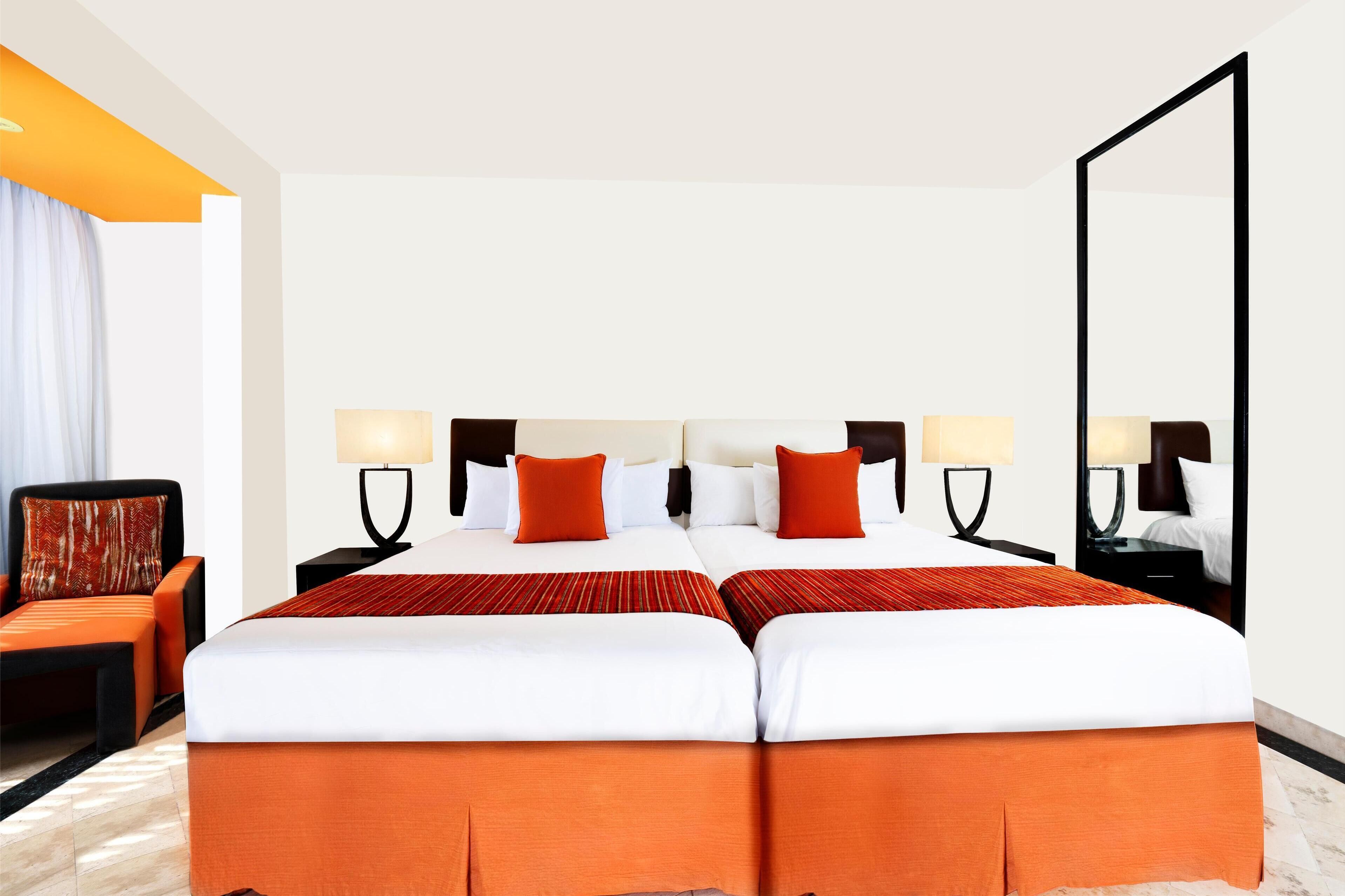 Een hotelkamer met een groot bed, twee nachtkastjes met lampen, een stoel en een grote spiegel.