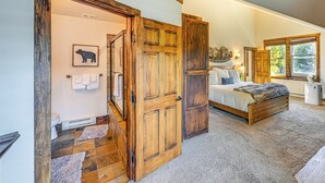Un dormitorio con puerta de madera, una cama, una ventana y un baño visible a través de una puerta abierta.