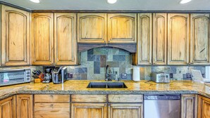 Una cocina con gabinetes de madera, encimera de granito, lavavajillas empotrado y salpicadero de piedra.