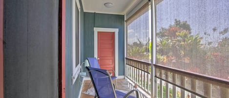 A balcony with a red door, a blue chair, and a view of greenery through a mesh screen.