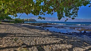 A beach with a rocky shoreline, a large cruise ship in the background, and a building with a sloped roof. - Oceanfront Kailua-kona Islander Studio w/ Lanai! (Kailua-Kona)