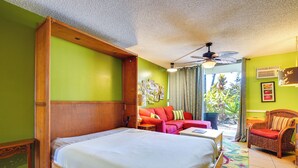 A hotel room with a large bed, a red sofa, a wicker chair, and a ceiling fan. - Oceanfront Kailua-kona Islander Studio w/ Lanai! (Kailua-Kona)