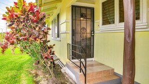 A yellow building with a black door and windows, a small porch, and a tree with red leaves. - Charming Historic Hilo House Minutes to Beach! (Hilo)