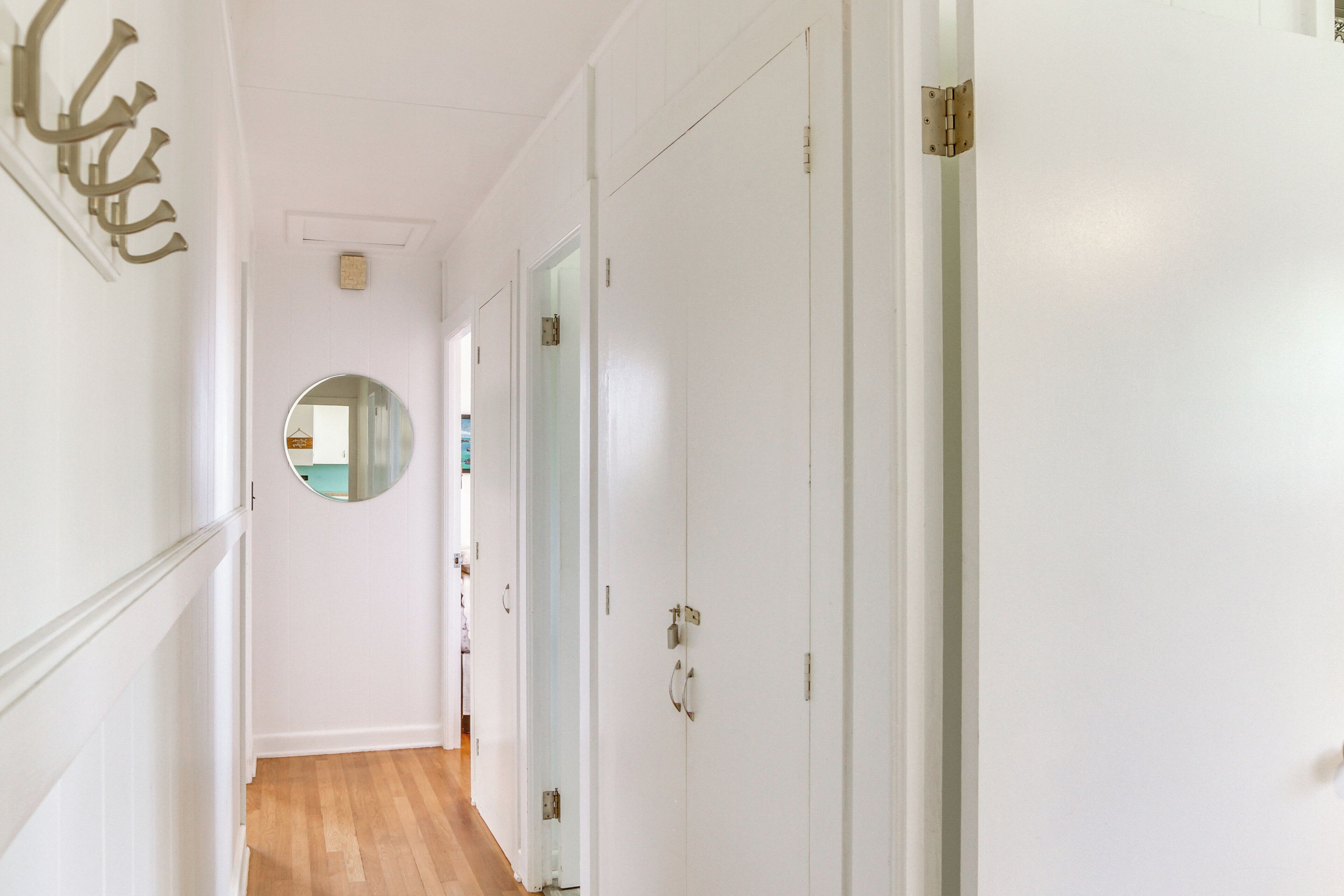 A hallway with white walls, a wooden floor, and a round mirror on the left.