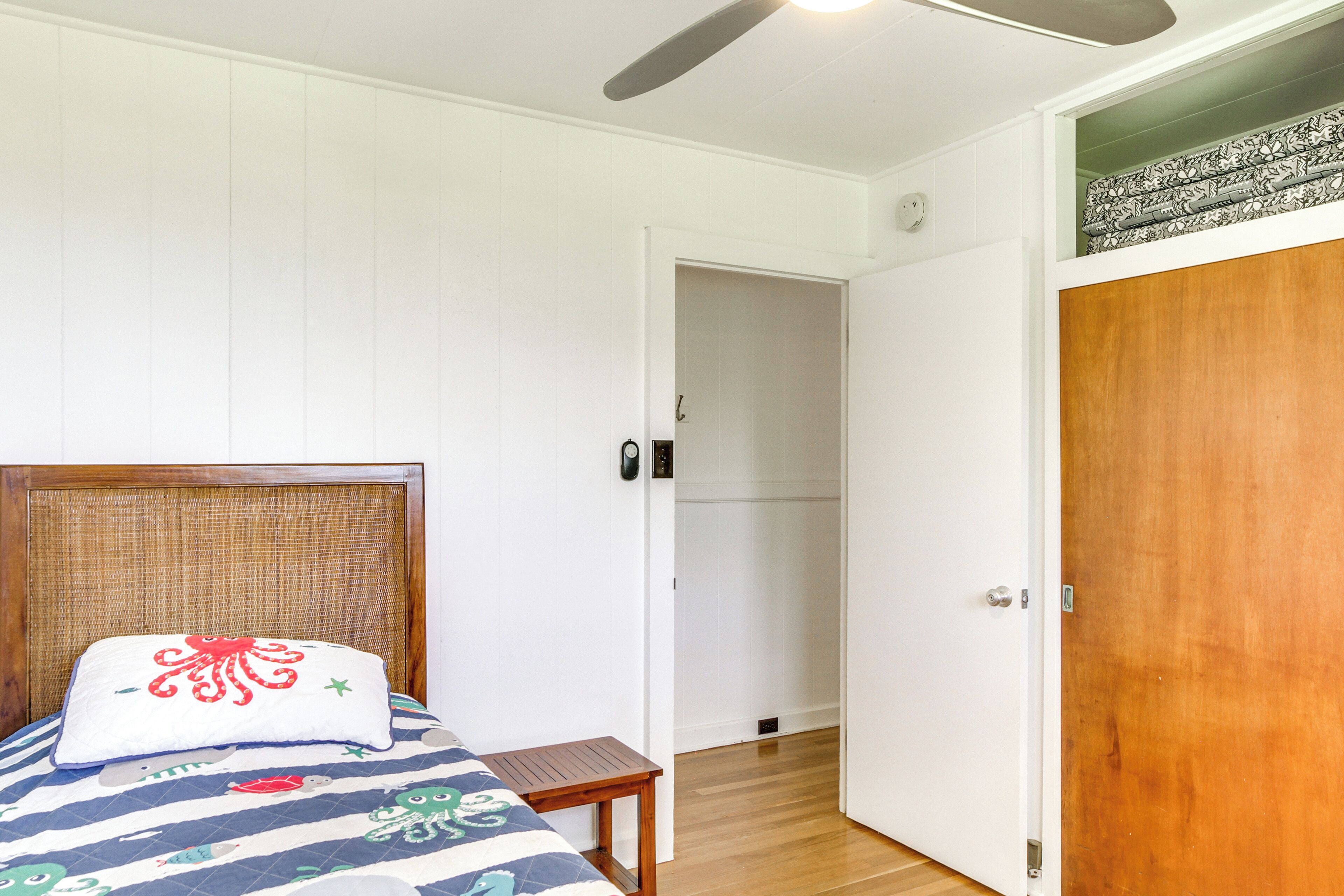 A bedroom with a bed, a bedside table, a wooden door, and a white wall.