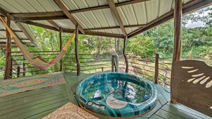 A hot tub under a wooden pergola with a hammock and a patterned mat on a wooden deck. - Tropical Cabana w/ Deck, Hot Tub & Lush Scenery! (Keaau)