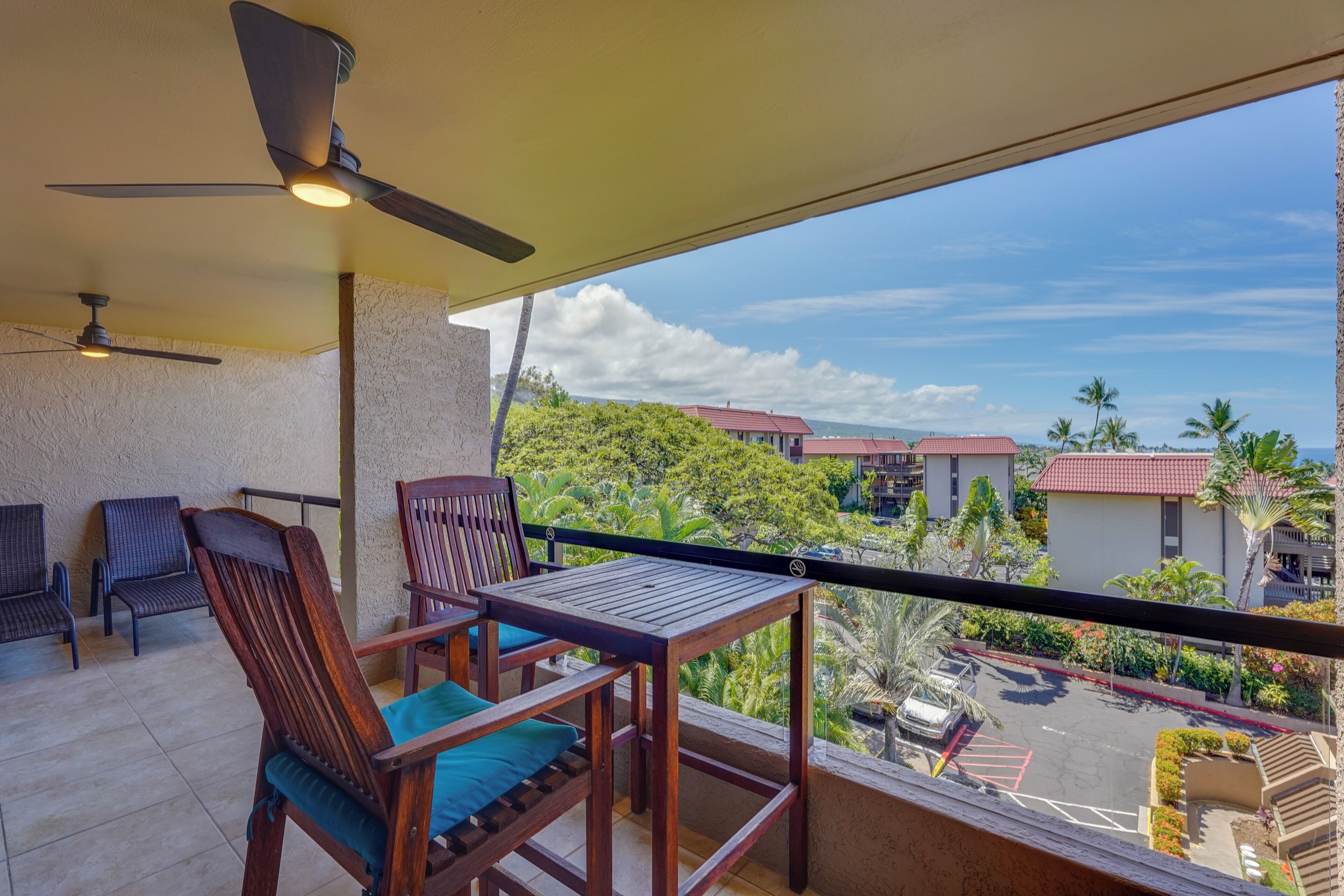 Un balcon avec une table et des chaises, un ventilateur de plafond et une vue sur les bâtiments et les arbres.