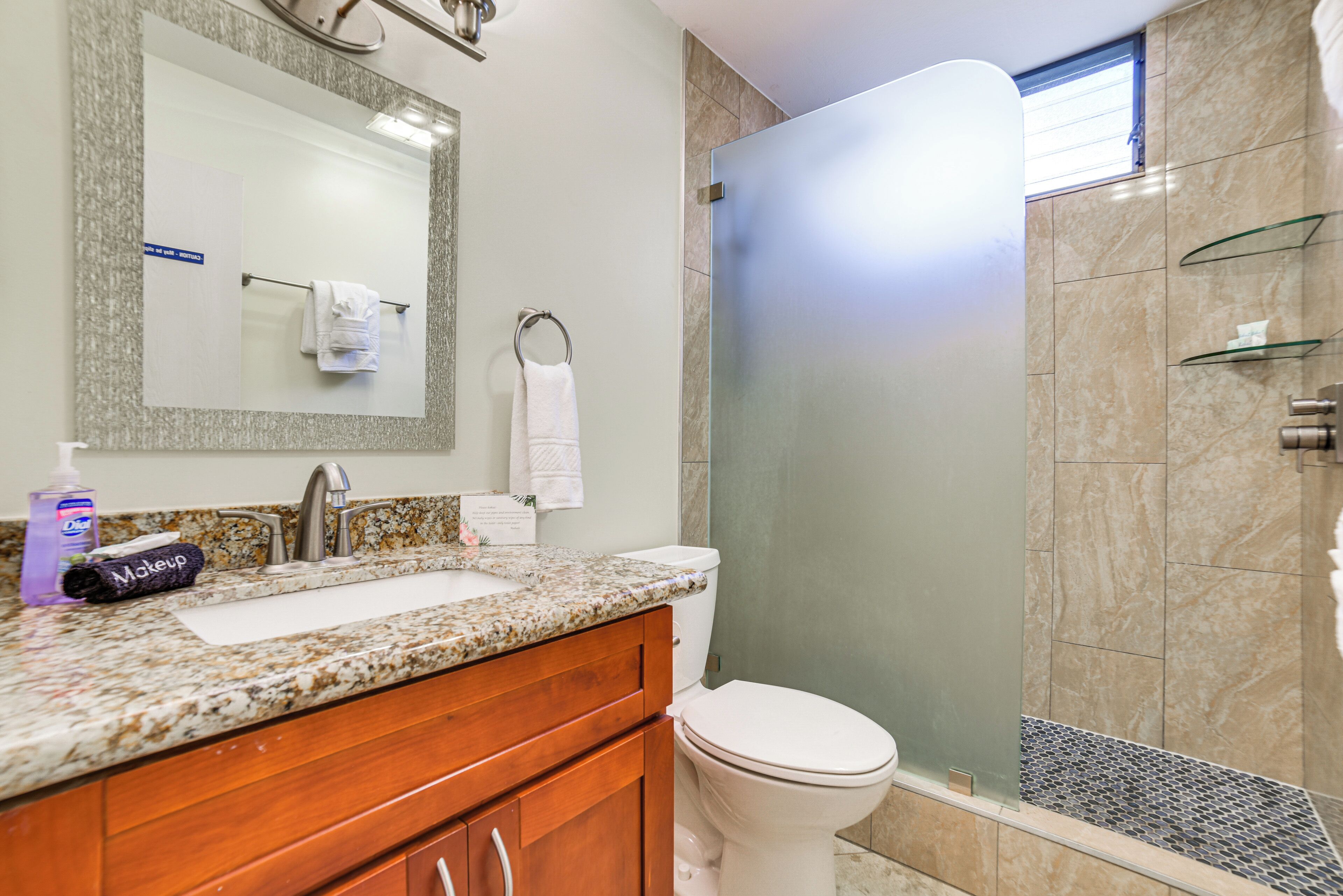 A bathroom with a granite countertop, a white sink, a mirror, a towel rack, and a glass shower enclosure.
