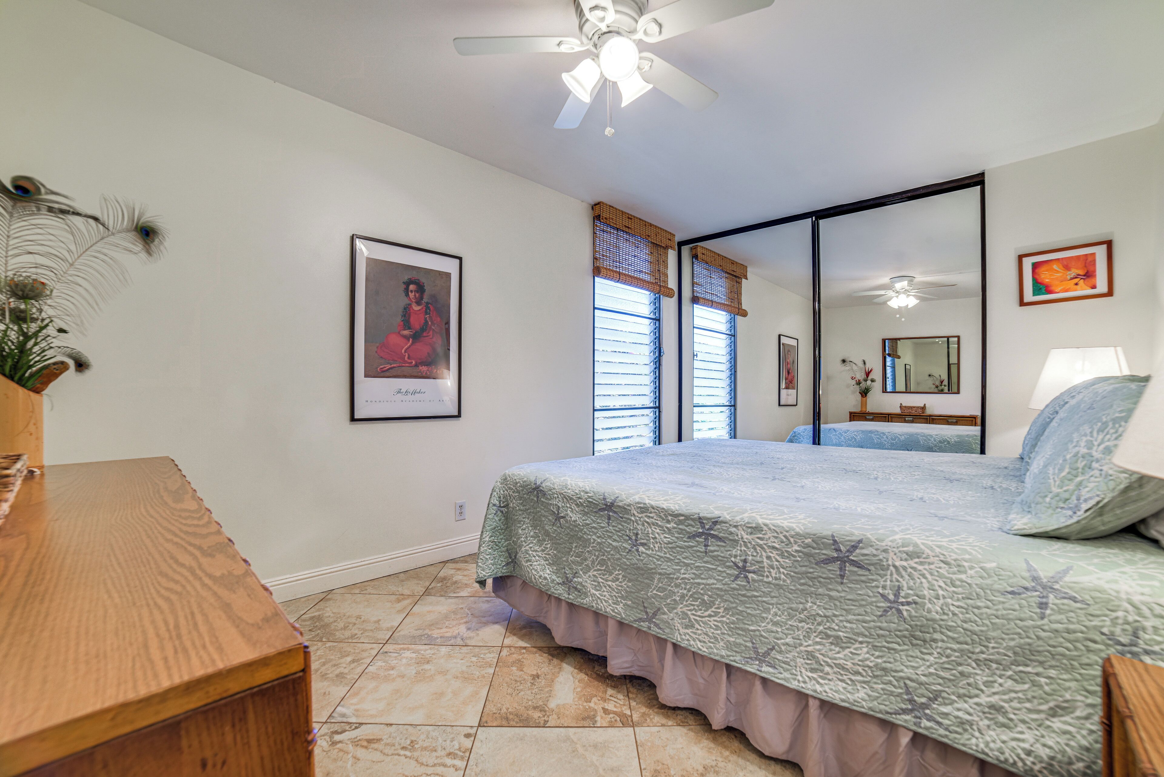 A bedroom with a bed, a ceiling fan, a window with blinds, a framed picture on the wall, and a wooden dresser.