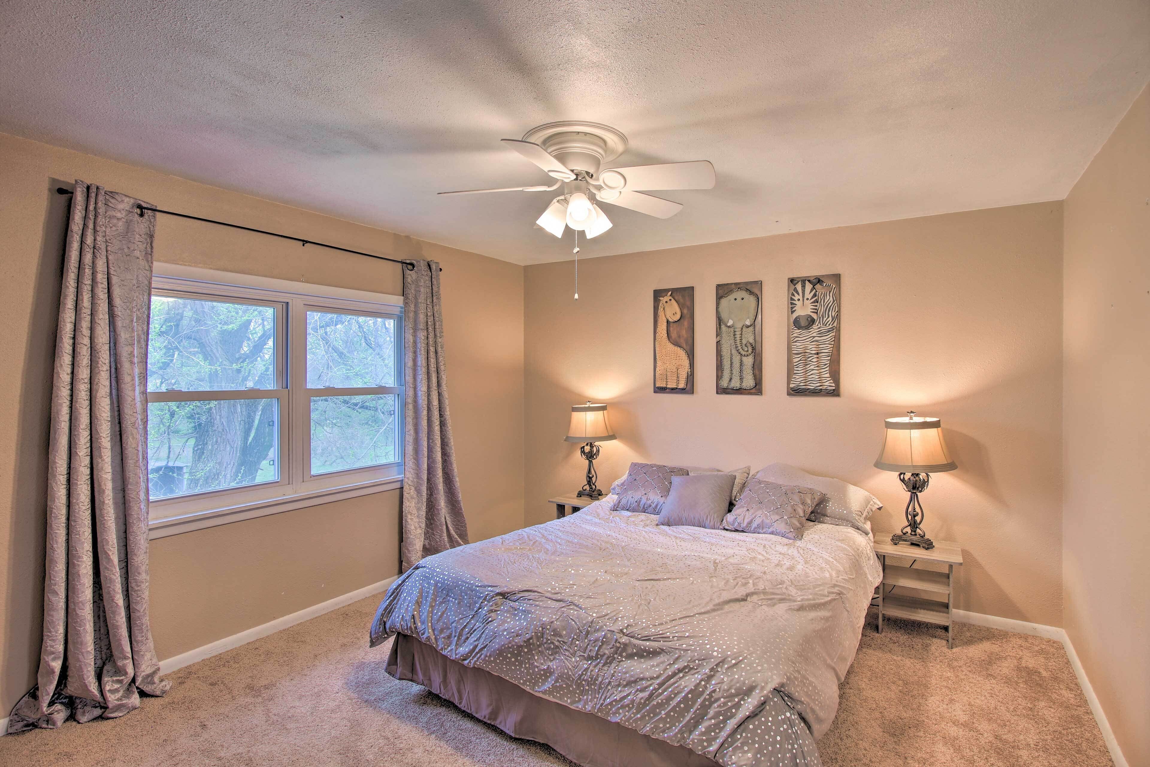 A bedroom with a bed, two bedside lamps, a ceiling fan, and a window with curtains.