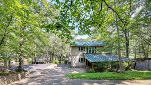 Une maison à deux étages, avec un toit en métal, entourée d’arbres et une allée menant à la porte d’entrée.