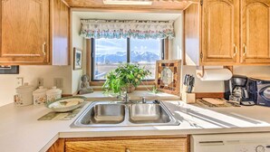 Una cocina con armarios de madera, un lavamanos doble, una ventana con vistas a las montañas y una planta en el alféizar.
