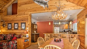 A cozy cabin interior with a dining area, wooden walls, and a ceiling-mounted elk antler chandelier. - Cabin < 2 Mi to Tahoe Donner Downhill Ski Resort (Truckee)