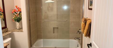 A bathroom with a glass-enclosed shower, a white bathtub, a toilet, and a sink.