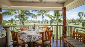 A covered outdoor dining area with a table set for two, chairs, a ceiling fan, and a view of a golf course and palm trees.