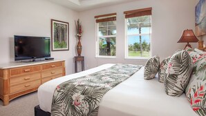 A bedroom with a bed, a TV on a wooden dresser, and two windows with blinds.