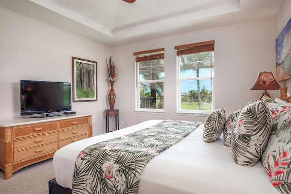 A bedroom with a bed, a TV on a wooden dresser, and two windows with blinds.