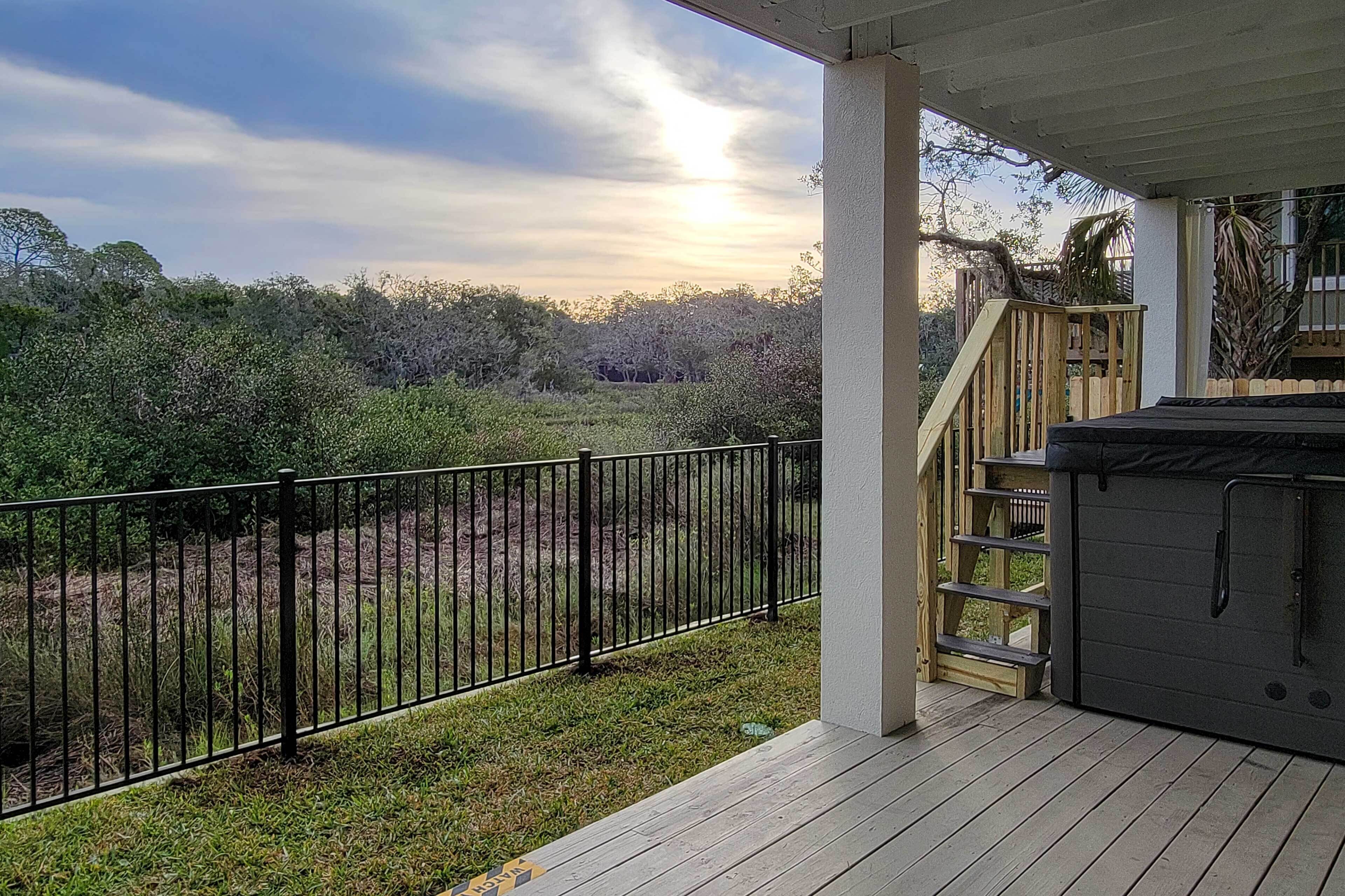 A deck with a hot tub, a wooden staircase, and a metal fence overlooking a wooded area.