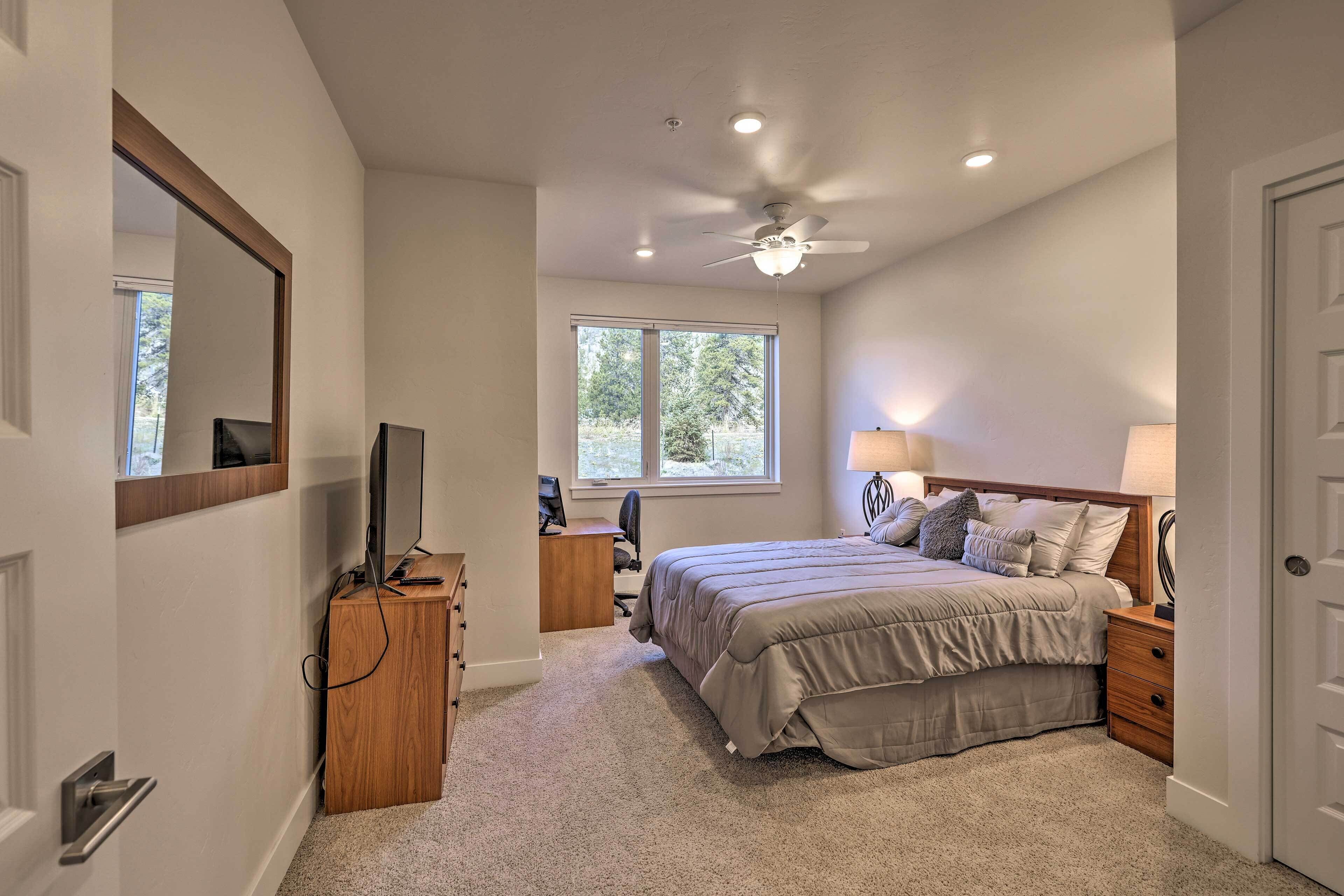 Une chambre à coucher comprenant un lit, des tables de chevet, un bureau, une chaise, un ventilateur de plafond et une fenêtre.