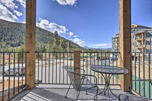 A balcony with a metal table and chair, overlooking a parking lot and a mountainous landscape.