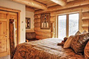 A log cabin bedroom with a large bed, a wooden headboard, a framed picture on the wall, and a window with a view of the forest. - 7 Mi to Granby Ranch: Secluded Cabin w/ Mtn Views! (Granby)