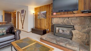 A cozy living room with a stone fireplace, leather sofa, and a mounted flat-screen TV. - Winter Park Condo w/ Hot Tubs, 4 Mi to Ski Resort! (Winter Park)