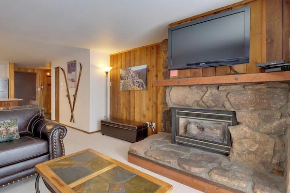 A cozy living room with a stone fireplace, leather sofa, and a mounted flat-screen TV. - Winter Park Condo w/ Hot Tubs, 4 Min to Ski Resort (Winter Park)
